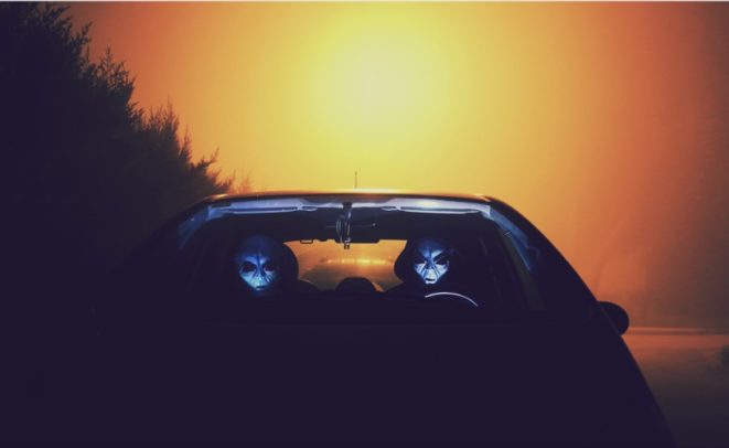 two stereotypical alien grays sitting in a car at sunset