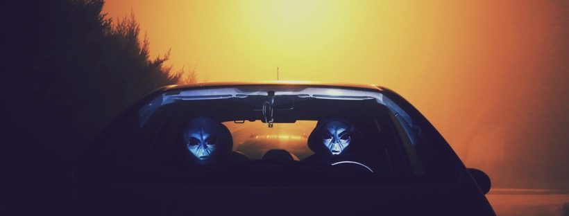 two stereotypical alien grays sitting in a car at sunset