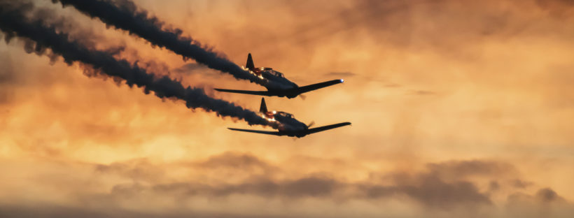 two single-engine aircraft flying toward the horizon against the backdrop of a sunset